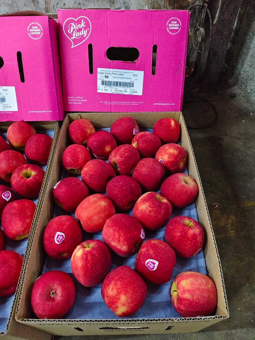An open carton of red apples with a pink carton lid behind it