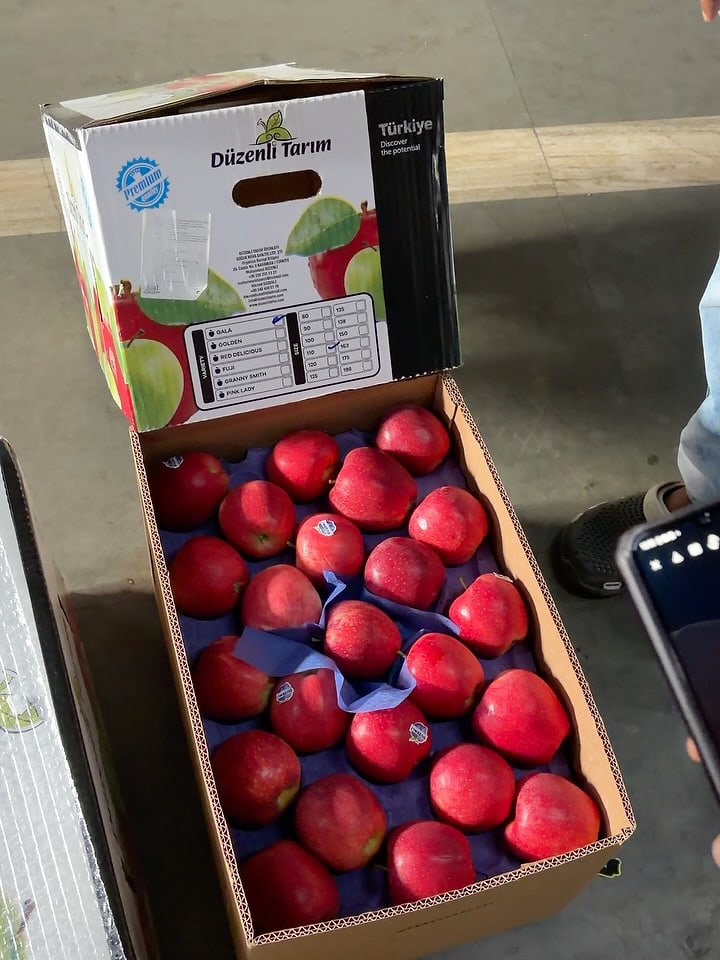 An apple carton with its lid raised, standing on a loading floor